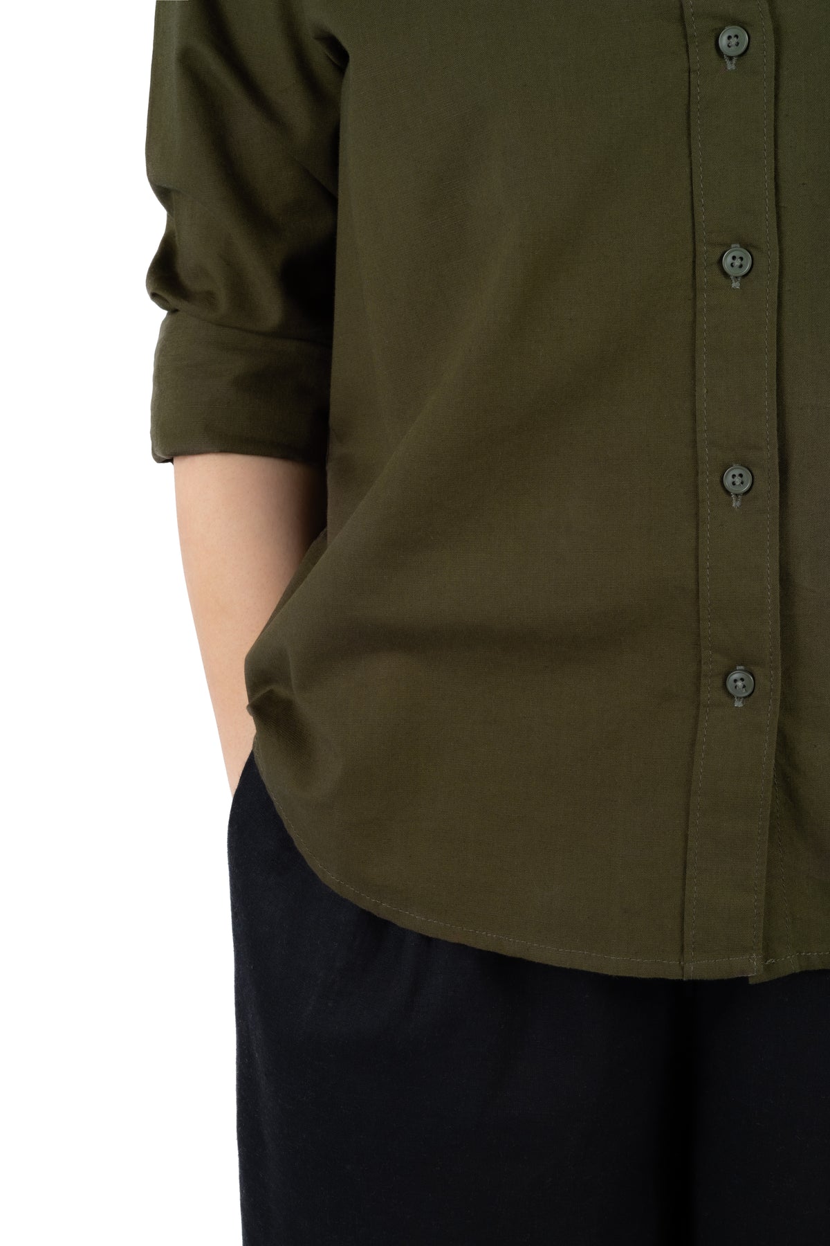 Close-up of a person wearing an olive green button-front shirt with rolled sleeves and dark pants against a plain white background.