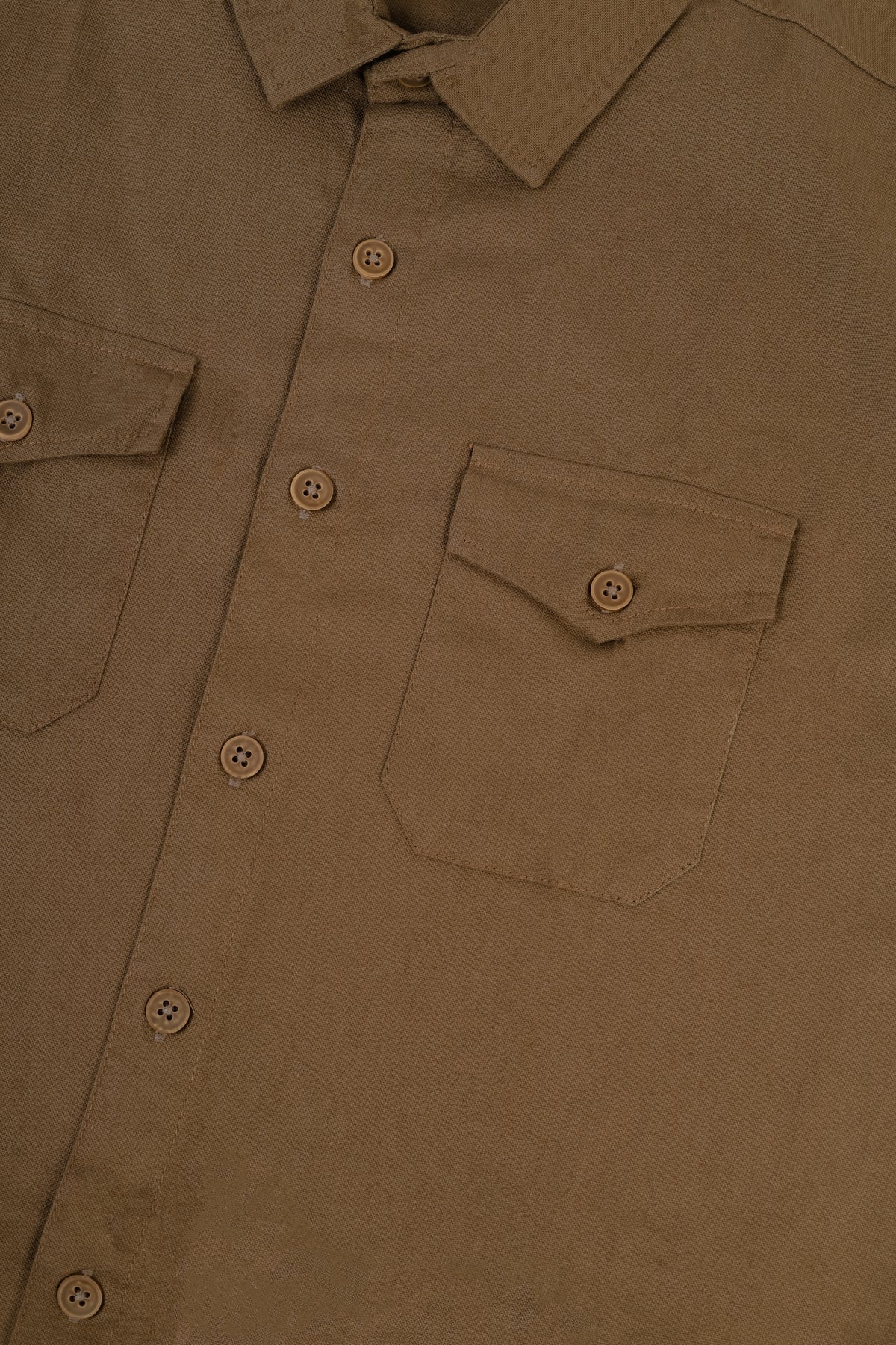 Close-up of a brown button-up shirt showing the chest pocket, button details, and textured fabric.