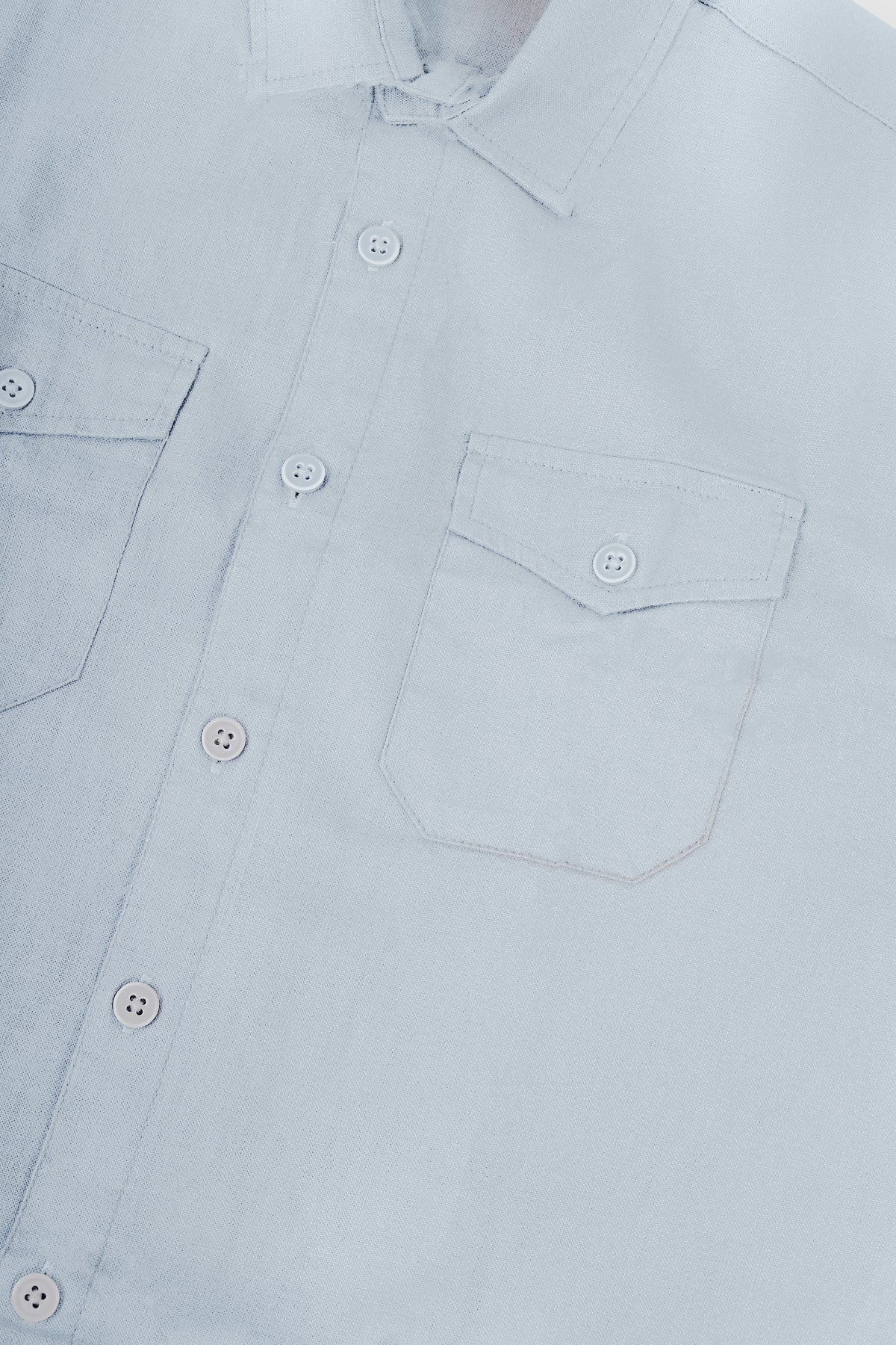 Close-up of a light blue button-down shirt showing the collar, front button placket, and chest pocket details.