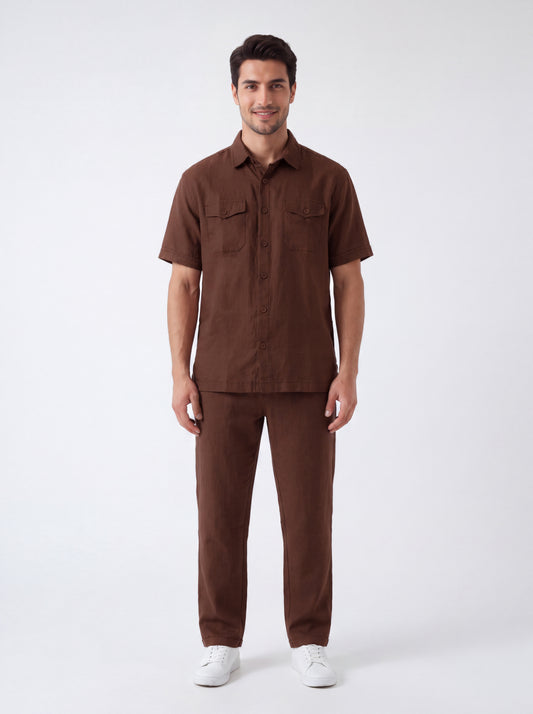 A man modeling a matching brown short-sleeve button-up shirt and trousers set, paired with white sneakers, against a plain light gray studio background.