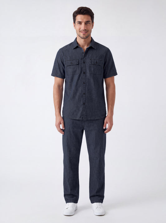 A man modeling a dark navy blue short-sleeve button-up shirt and matching dark navy pants, paired with white sneakers, against a plain light gray studio background.
