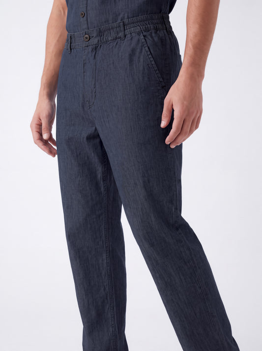 A close-up of a person wearing dark navy blue denim work pants, showing the waist, front pockets, and legs against a plain white studio background.