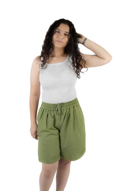 A woman modeling a pair of olive green drawstring shorts and a white tank top against a plain white background.