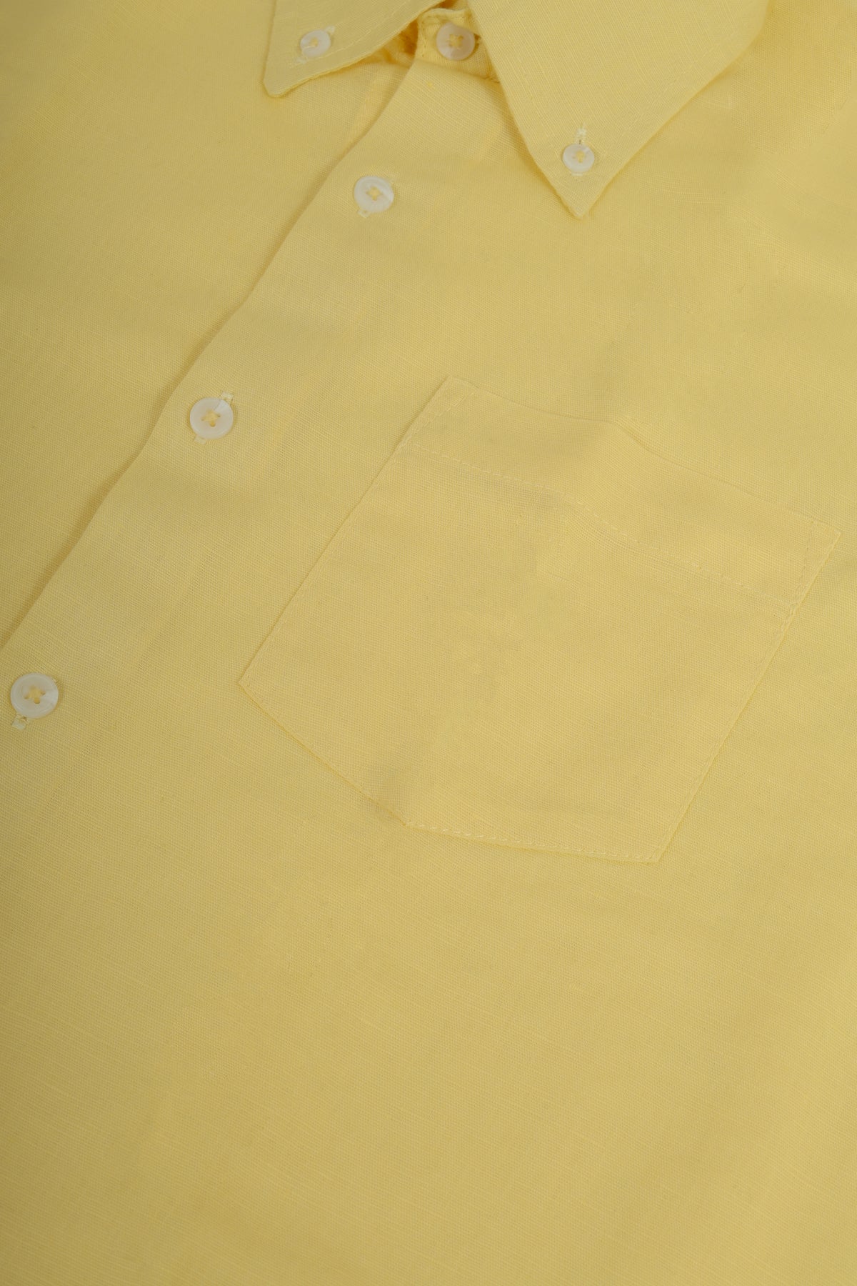 A close-up of a light yellow long-sleeve button-down shirt, showing the collar, white buttons, and a chest pocket.