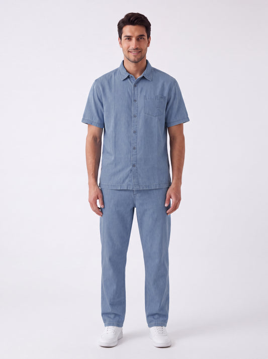 A man modeling a light blue short-sleeve button-up shirt and matching light blue pants against a plain white studio background.