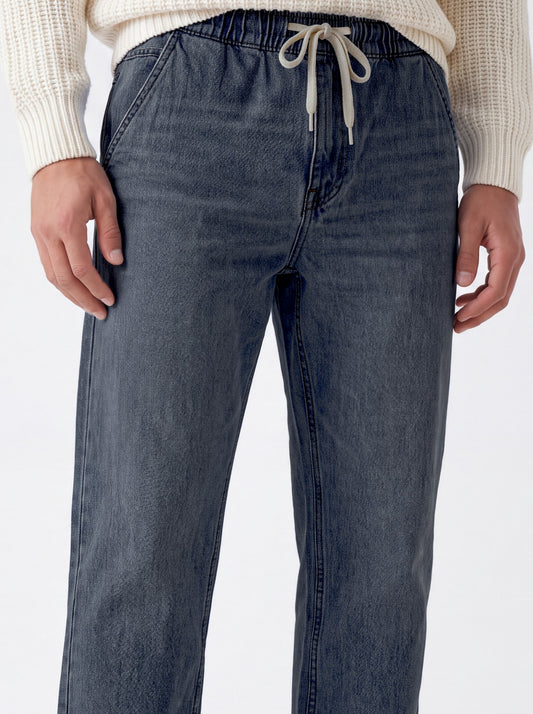 A close-up of a person wearing dark blue denim drawstring pants with a cream ribbed knit sweater, shown from the waist down against a plain white background.
