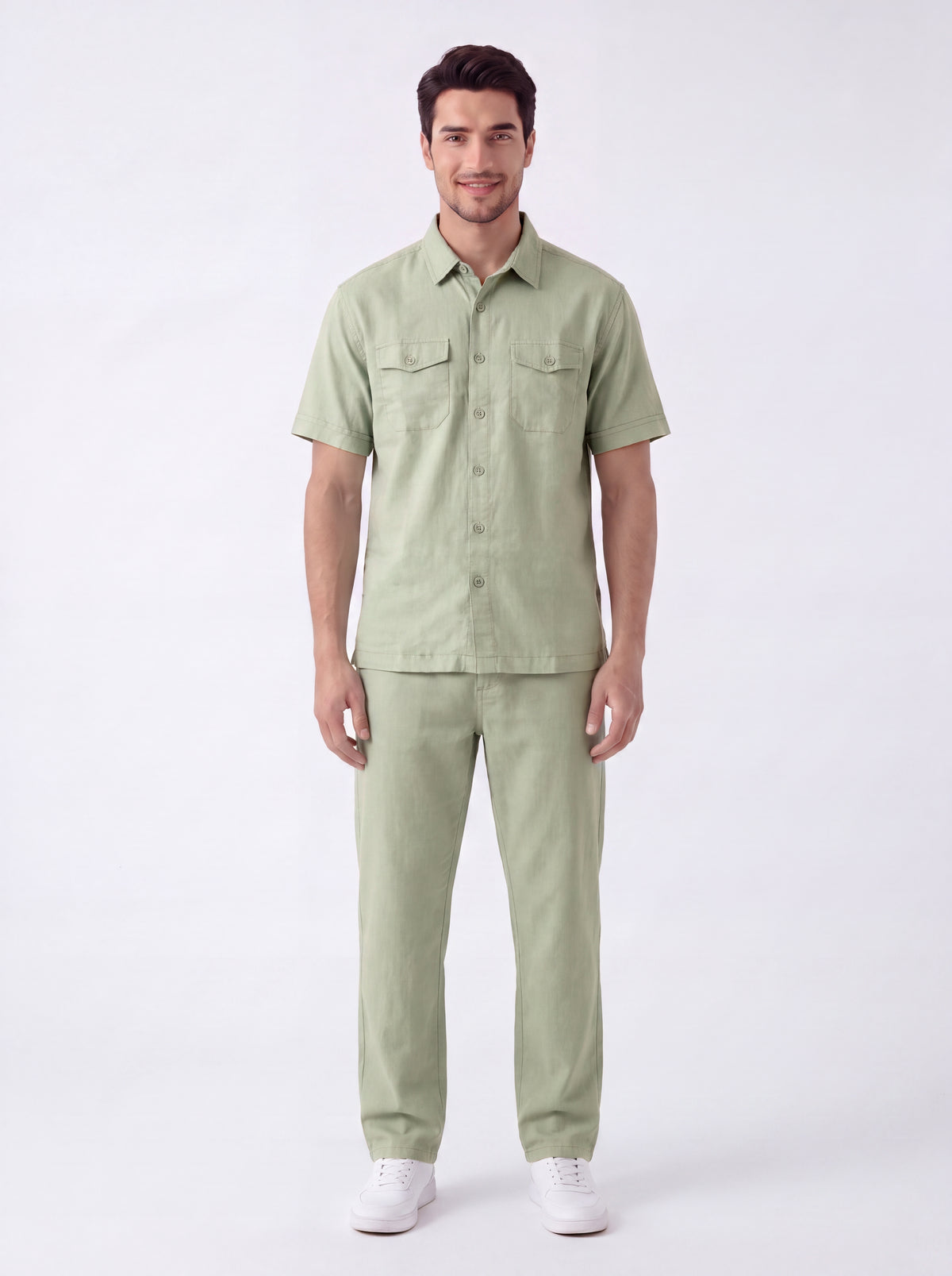 A man modeling a light sage green short-sleeve button-up shirt and matching trousers against a plain white studio background.