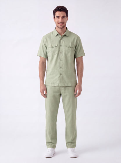 A man modeling a light sage green short-sleeve button-up shirt and matching trousers against a plain white studio background.