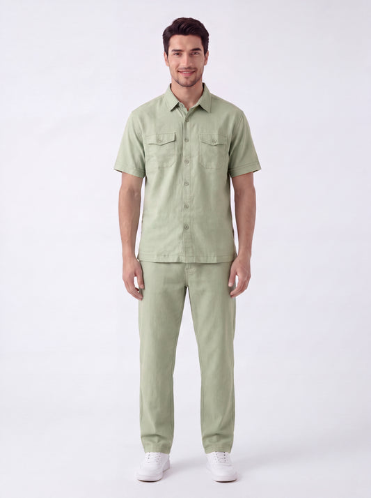 A man modeling a light sage green short-sleeve button-up shirt and matching trousers against a plain white studio background.