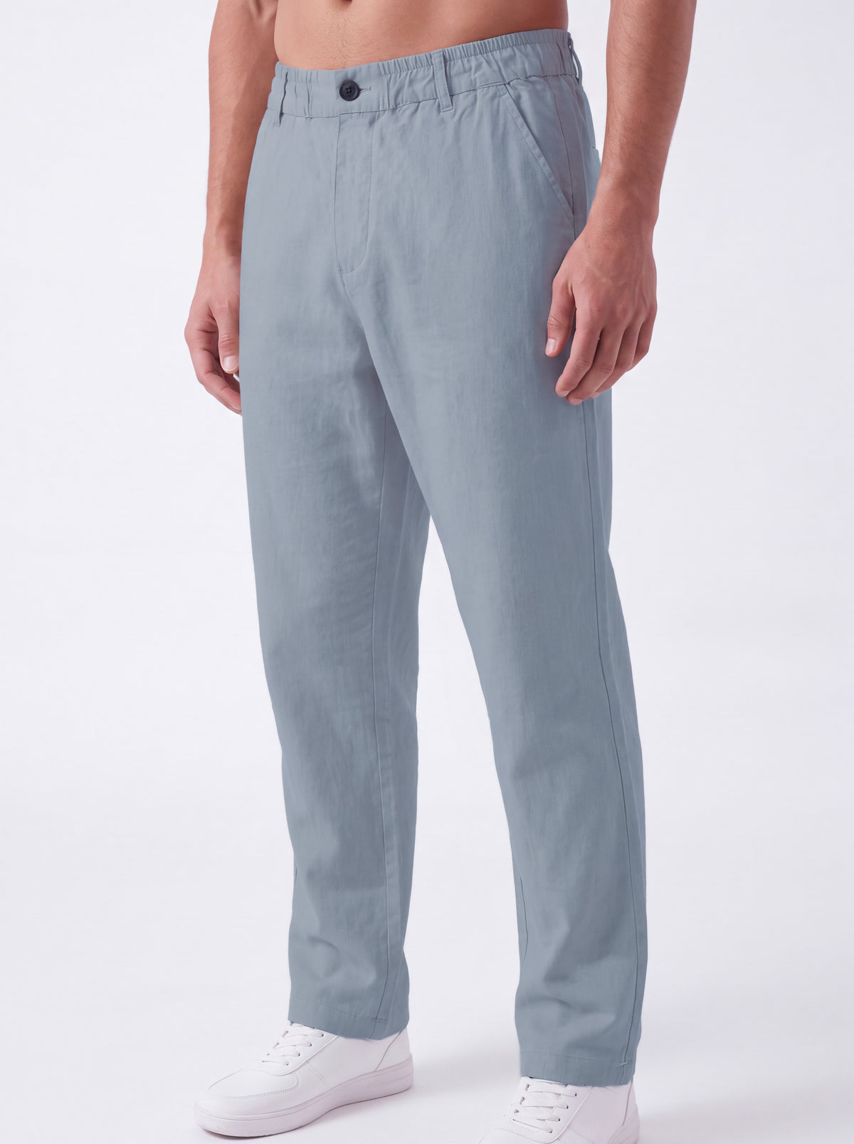 A person wearing light blue straight-leg trousers with a button waistband, paired with white sneakers, shown against a plain light gray studio background.