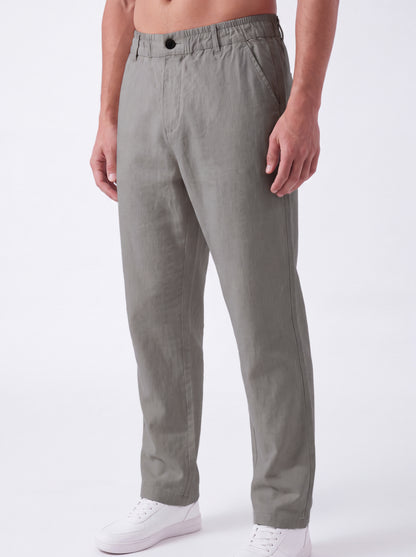 A person wearing light gray relaxed-fit trousers with white sneakers, shown from the waist down against a plain white studio background.