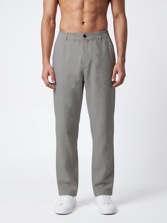 A man wearing light gray straight-leg trousers and white sneakers, standing against a plain light gray studio background.