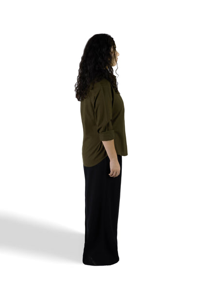 A woman shown from the side profile wearing a dark olive green long-sleeve top with rolled sleeves and a long black skirt, standing against a plain white studio background.