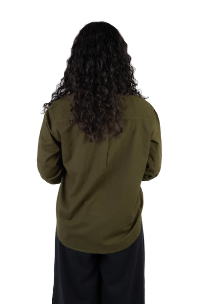 A person viewed from the back wearing a dark olive green long-sleeve shirt and black pants, with long dark curly hair, against a plain white background.