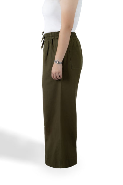 A side-profile view of a model wearing olive green wide-leg cropped pants with an elastic drawstring waistband and a side pocket, paired with a white sleeveless top against a white studio background.
