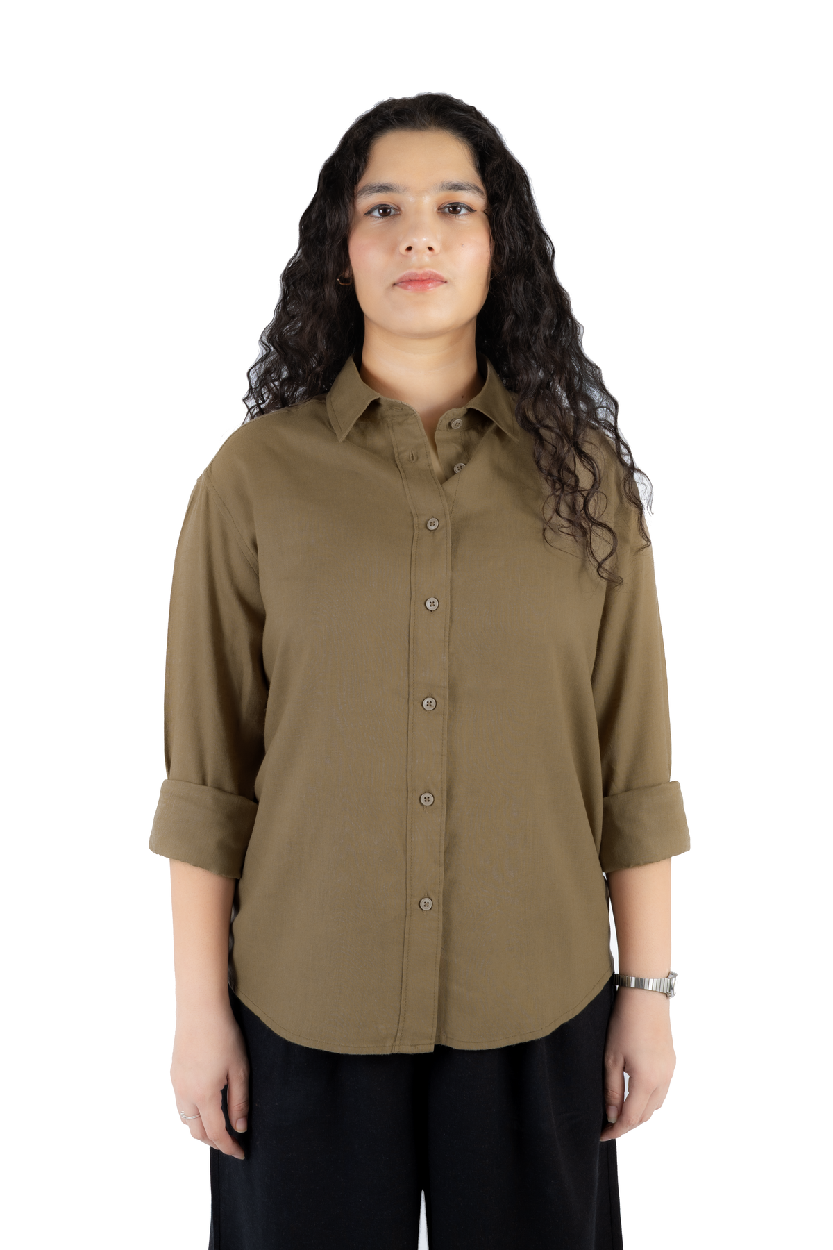 A woman with long, curly dark hair wearing a muted olive-brown button-up shirt with rolled sleeves and black pants, standing against a plain white background.