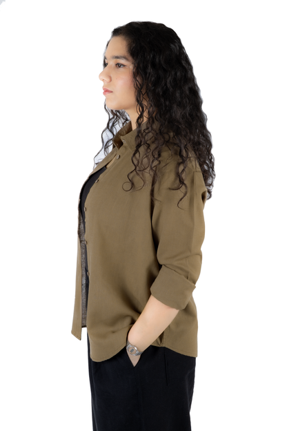 A woman with long, curly dark hair is shown in profile wearing a muted olive-brown button-up shirt with black pants, photographed against a solid white background.