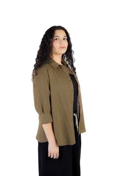 A woman with long, curly dark hair is shown in profile wearing an olive green button-up shirt over a black top and black pants, set against a plain white background.