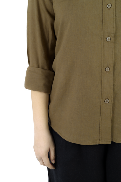 A close-up of a person wearing a muted olive-brown button-up shirt with rolled sleeves and dark pants, photographed against a plain white background.