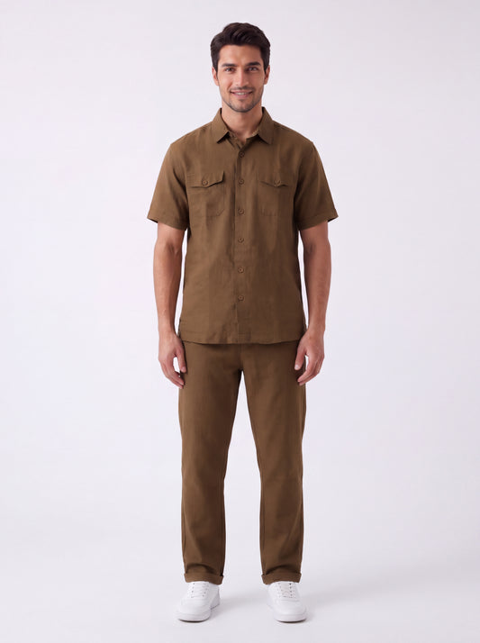 A man modeling a matching brown short-sleeve button-up shirt and trousers set, paired with white sneakers, against a plain white studio background.