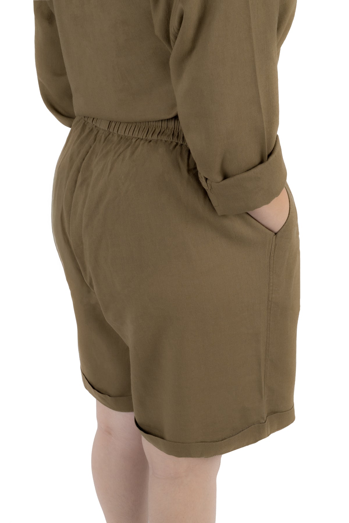 A close-up side view of a person wearing olive brown shorts with a gathered elastic waistband and side pockets, paired with a matching long-sleeve top against a plain white background.