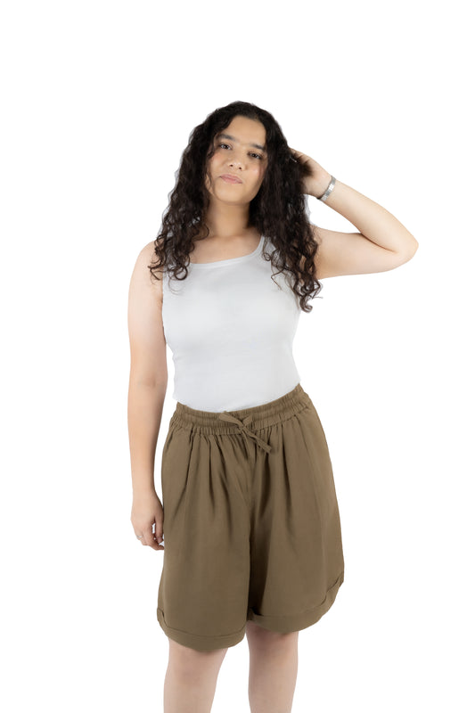 A woman modeling a white ribbed tank top and brown drawstring shorts against a solid white background.