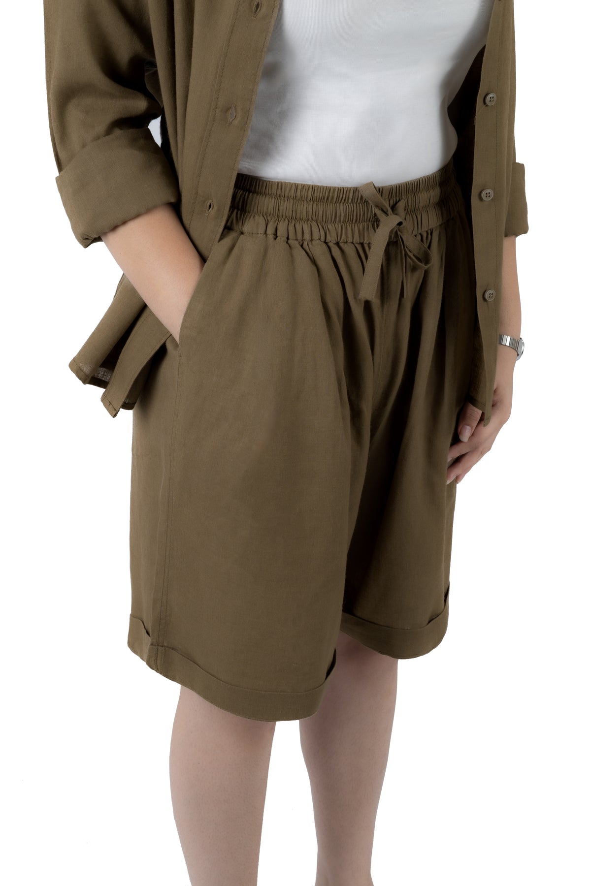 A person wearing olive brown drawstring shorts with a matching button-up shirt and white top, shown from the chest down against a plain white background.