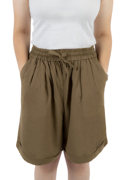A person wearing loose, high-waisted olive brown shorts with an elastic drawstring waistband, paired with a white sleeveless top, shown against a plain white background.