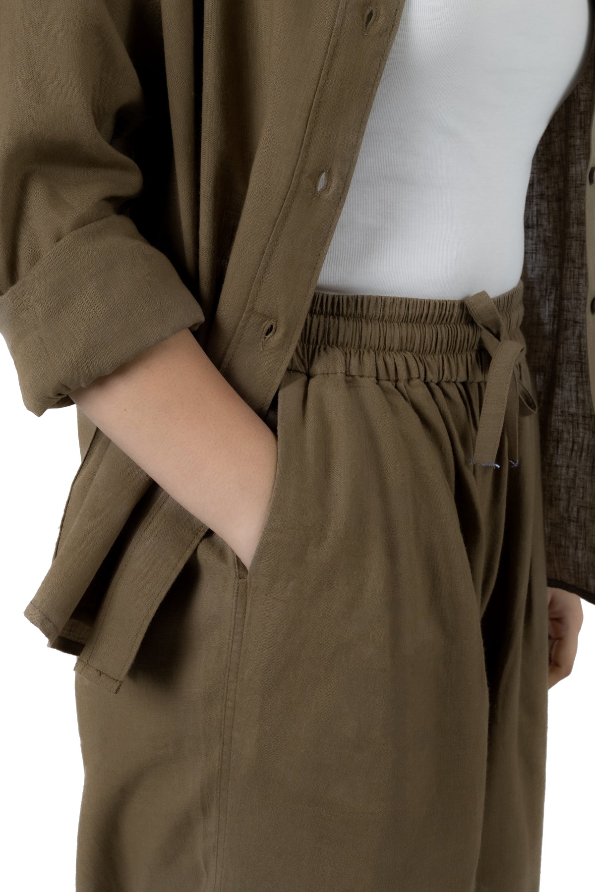 Close-up of a person wearing olive brown wide-leg trousers with an elastic waistband and drawstring, styled with a white top and an open olive brown shirt.