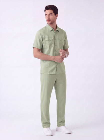 A man modeling a light sage green short-sleeve button-up shirt and matching trousers, paired with white sneakers, against a plain white studio background.