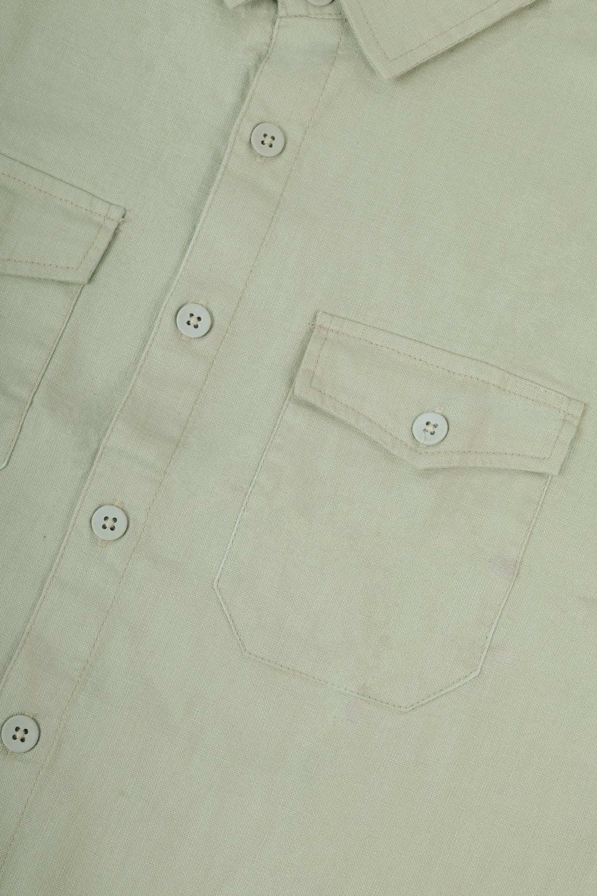 Close-up of a light sage green button-down shirt showing the chest pocket, button details, and fabric texture.