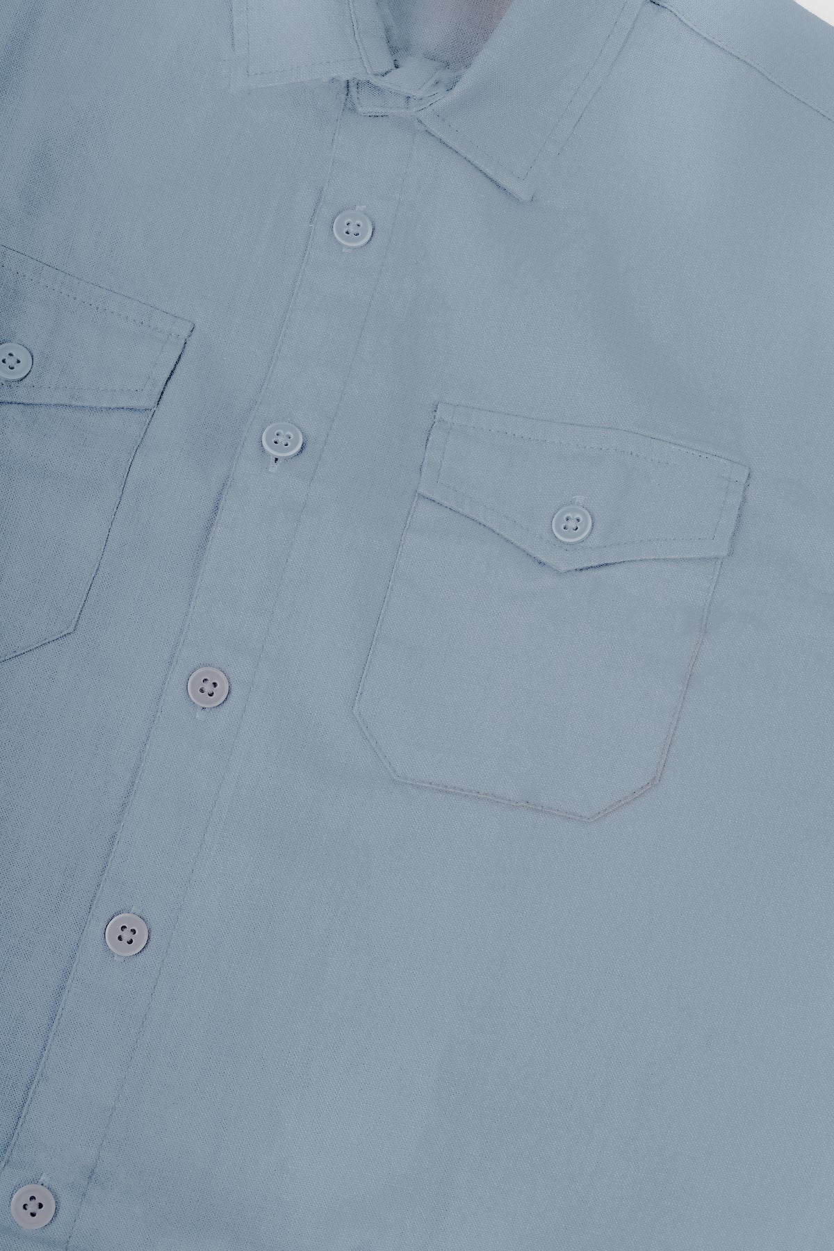 Close-up of a light blue button-down shirt showing the collar, front button placket, and left chest pocket.