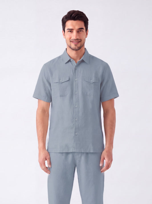 A man modeling a light blue short-sleeve button-up shirt and matching trousers against a plain light gray studio background.