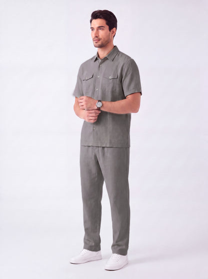 A man modeling a matching gray short-sleeve button-up shirt and trousers set, paired with white sneakers, against a plain light gray studio background.
