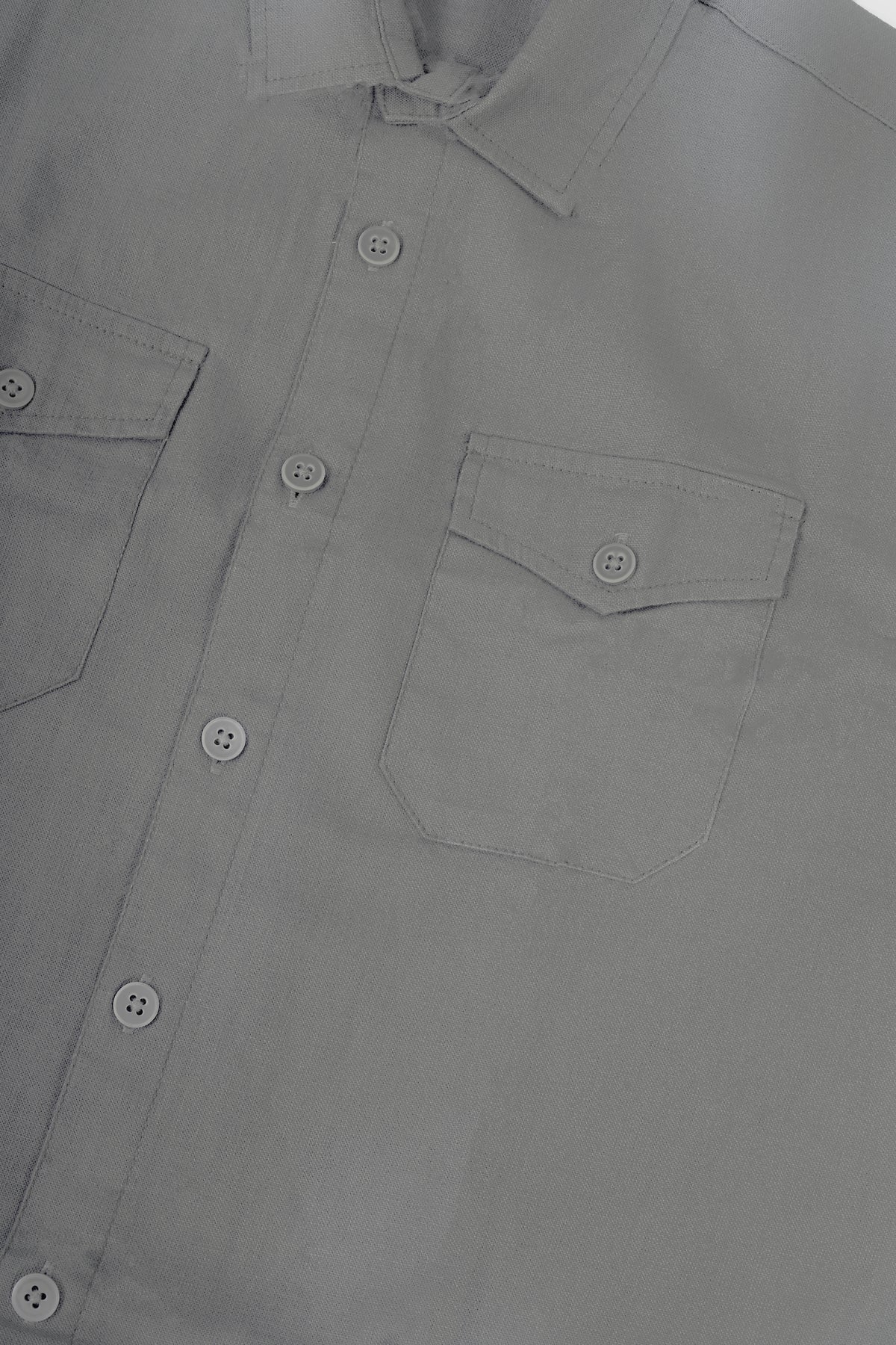 Close-up of a light gray button-down shirt showing the collar, front button placket, and left chest pocket with a button flap.