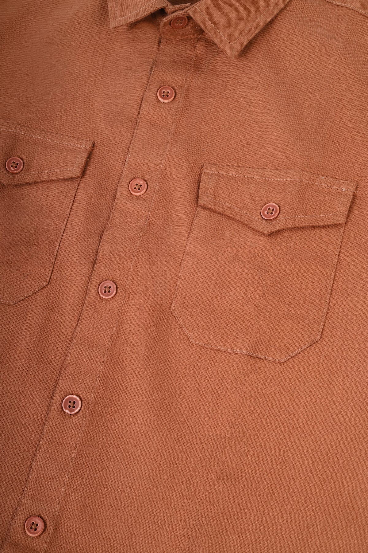 Close-up of a terracotta-colored button-down shirt showing the chest pocket, button closure, and collar.