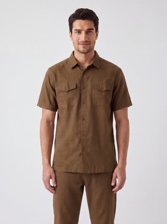 A man wearing a brown short-sleeve button-up shirt with two chest flap pockets and matching brown pants, standing against a light gray studio background.
