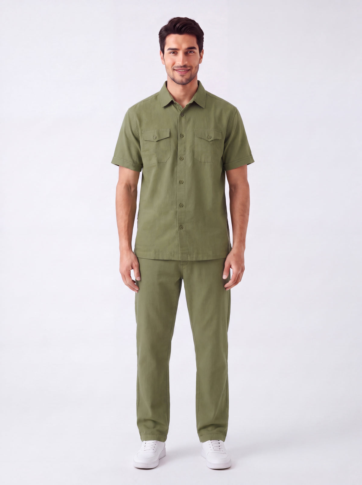 A man modeling a matching olive green short-sleeve button-up shirt and trousers set, paired with white sneakers, against a plain white studio background.