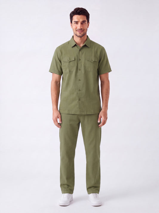 A man modeling a matching olive green short-sleeve button-up shirt and trousers set, paired with white sneakers, against a plain white studio background.