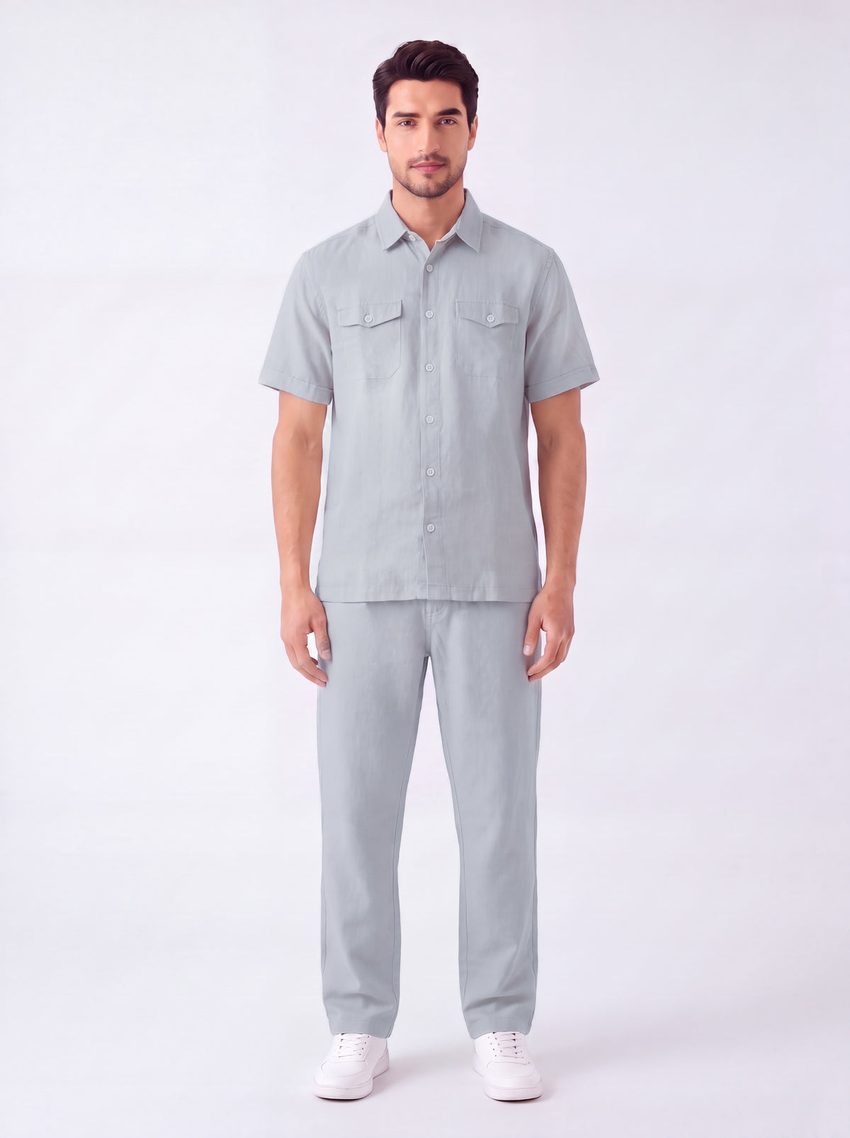 A man modeling a light gray short-sleeve button-up shirt and matching light gray trousers, paired with white sneakers, against a plain white studio background.