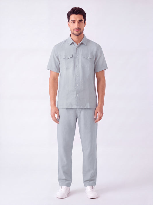 A man modeling a light gray short-sleeve button-up shirt and matching light gray trousers, paired with white sneakers, against a plain white studio background.
