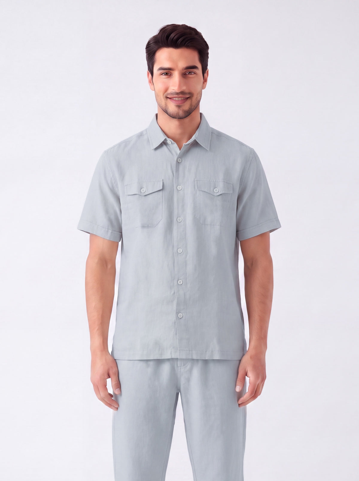 A man modeling a light gray short-sleeve button-up shirt and matching gray pants against a plain light gray studio background.
