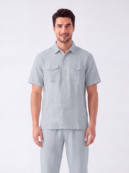 A man modeling a light gray short-sleeve button-up shirt and matching gray pants against a plain light gray studio background.