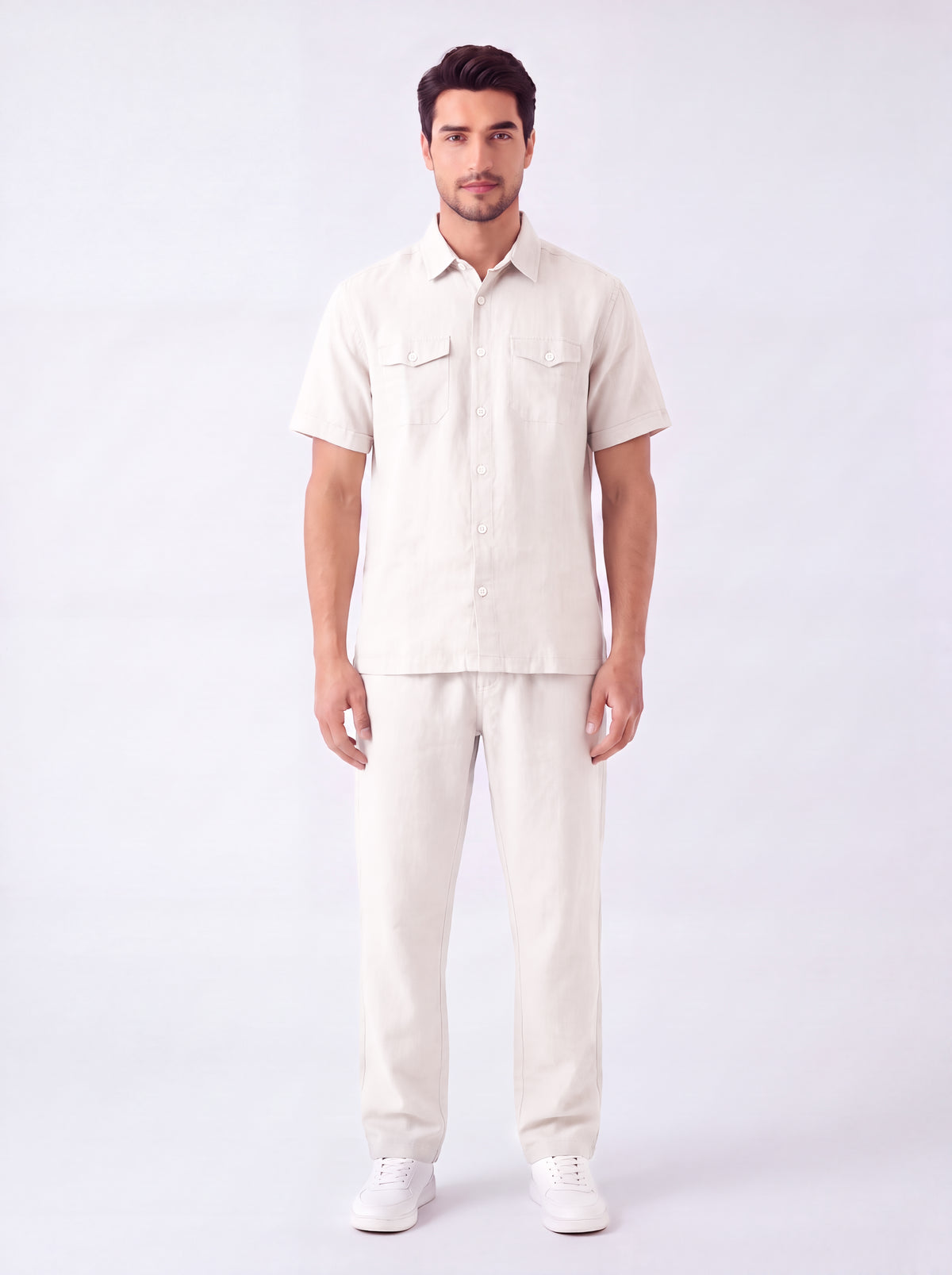 A man modeling a light beige short-sleeve button-up shirt and matching beige trousers against a plain white studio background.