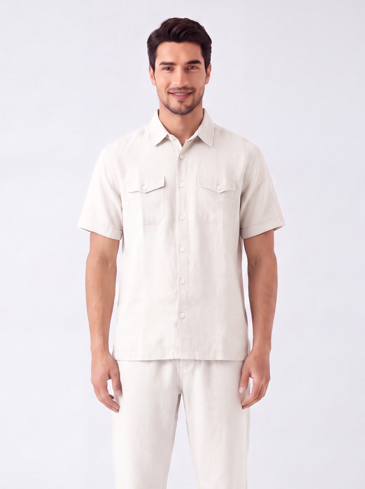 A man modeling a short-sleeve button-up shirt and matching light beige pants against a plain light gray studio background.