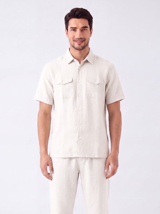 A man modeling a short-sleeve button-up shirt and matching light beige pants against a plain light gray studio background.