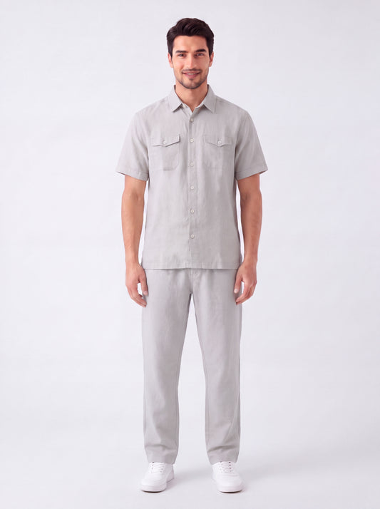 A man modeling a light gray short-sleeve button-up shirt and matching light gray trousers against a plain white studio background.