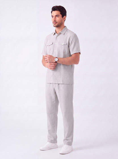 A man modeling a light gray short-sleeve button-up shirt and matching light gray trousers, paired with white sneakers, against a plain white studio background.