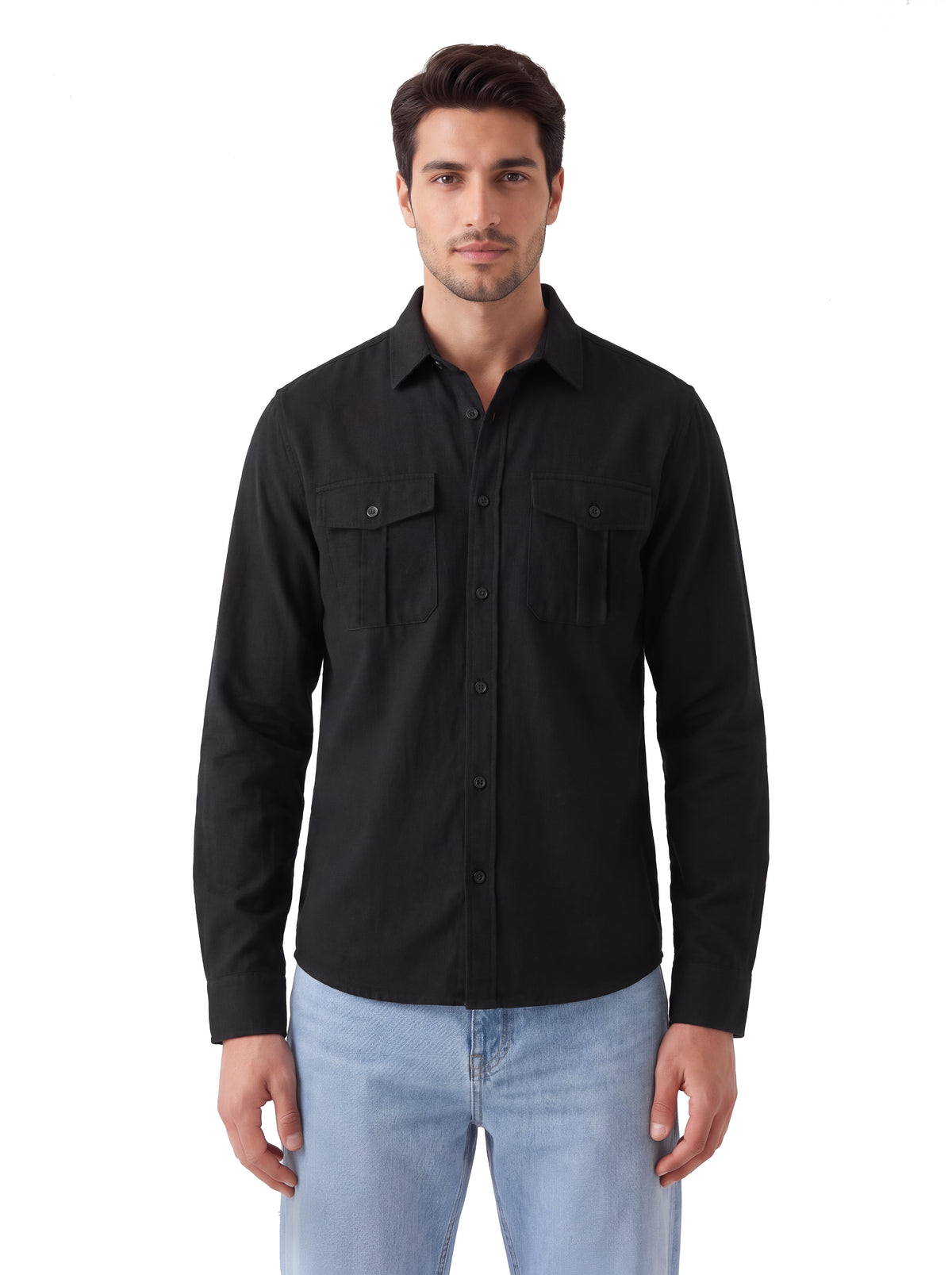 A man wearing a black long-sleeve button-up shirt with two chest flap pockets and light blue jeans, standing against a plain white background.
