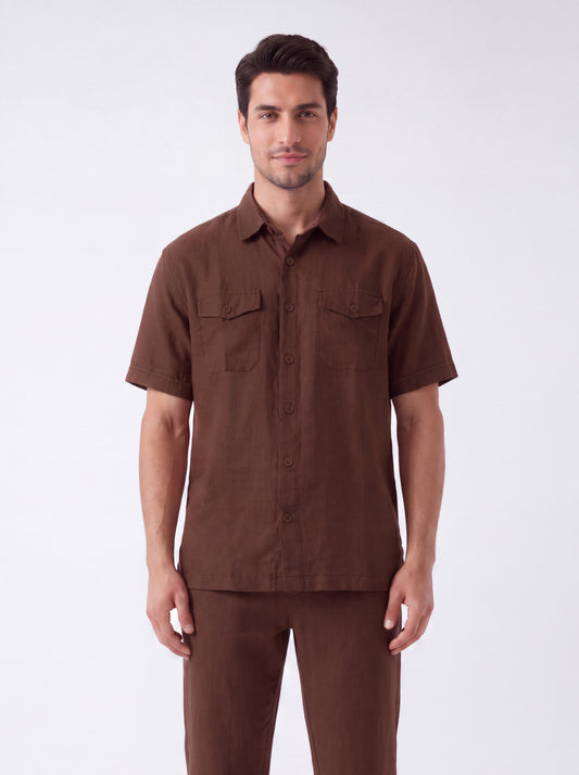 A man modeling a brown short-sleeve button-up shirt with two chest flap pockets, paired with matching brown trousers, against a plain light gray studio background.